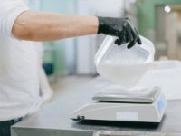 person pouring an ingredient from a plastic container to a weighing scale