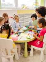 children sitting on chairs in front of table with art materials