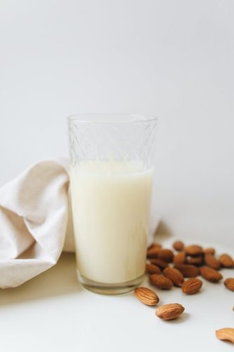 milk in clear drinking glass beside brown coffee beans